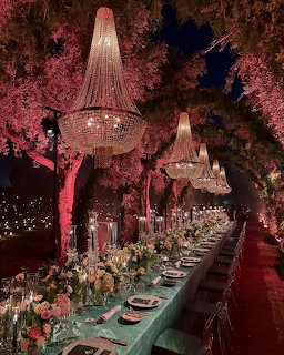Long outdoor dining table with crystal chandeliers and pink blossoming trees at night