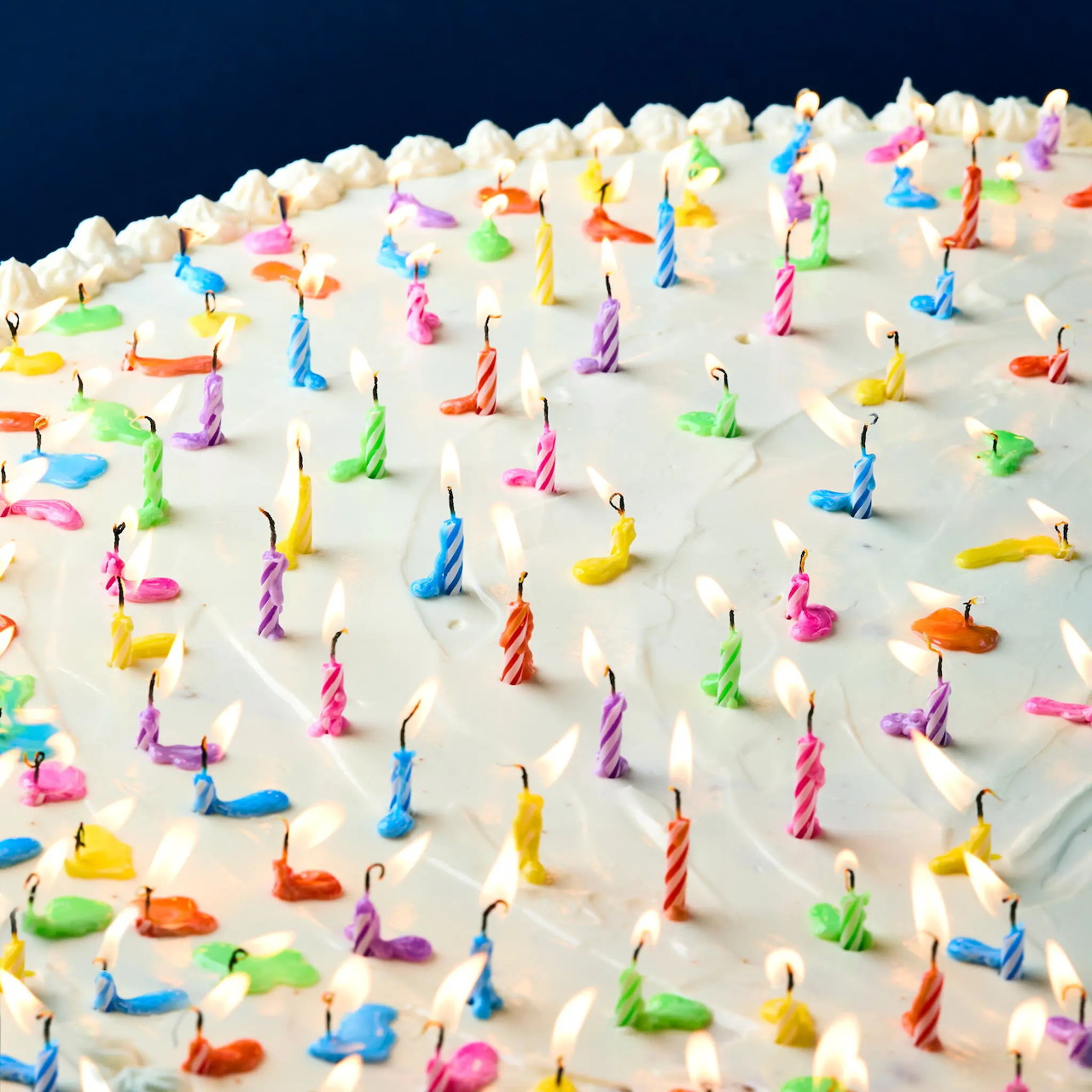 White birthday cake topped with numerous rainbow-colored spiral candles arranged in rows