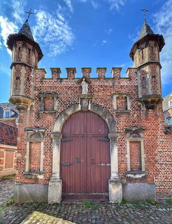 Large wooden arched door in a red brick gatehouse with two small turrets and battlements