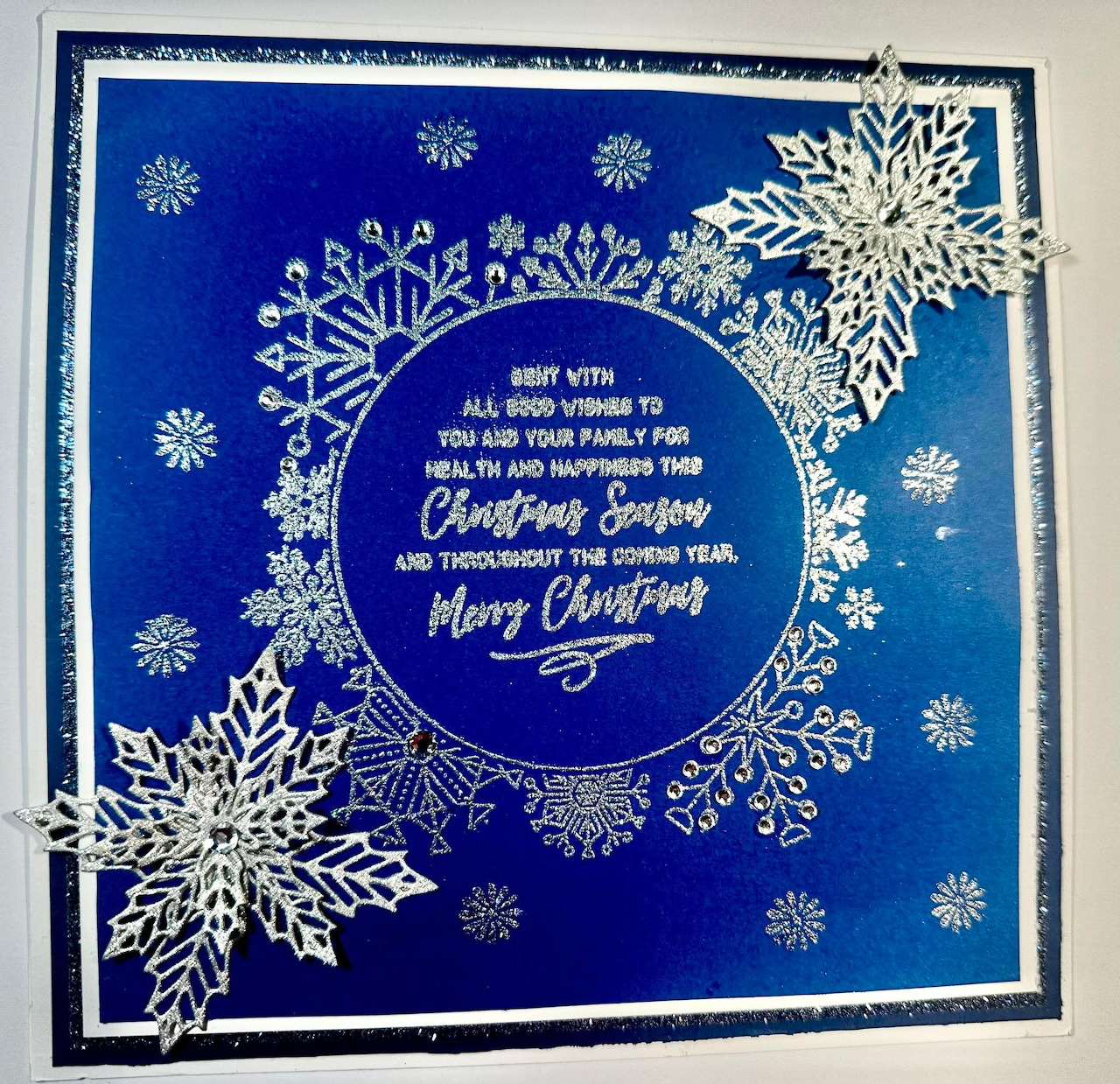 Blue handmade Christmas card with white snowflake decorations and a circular holiday message