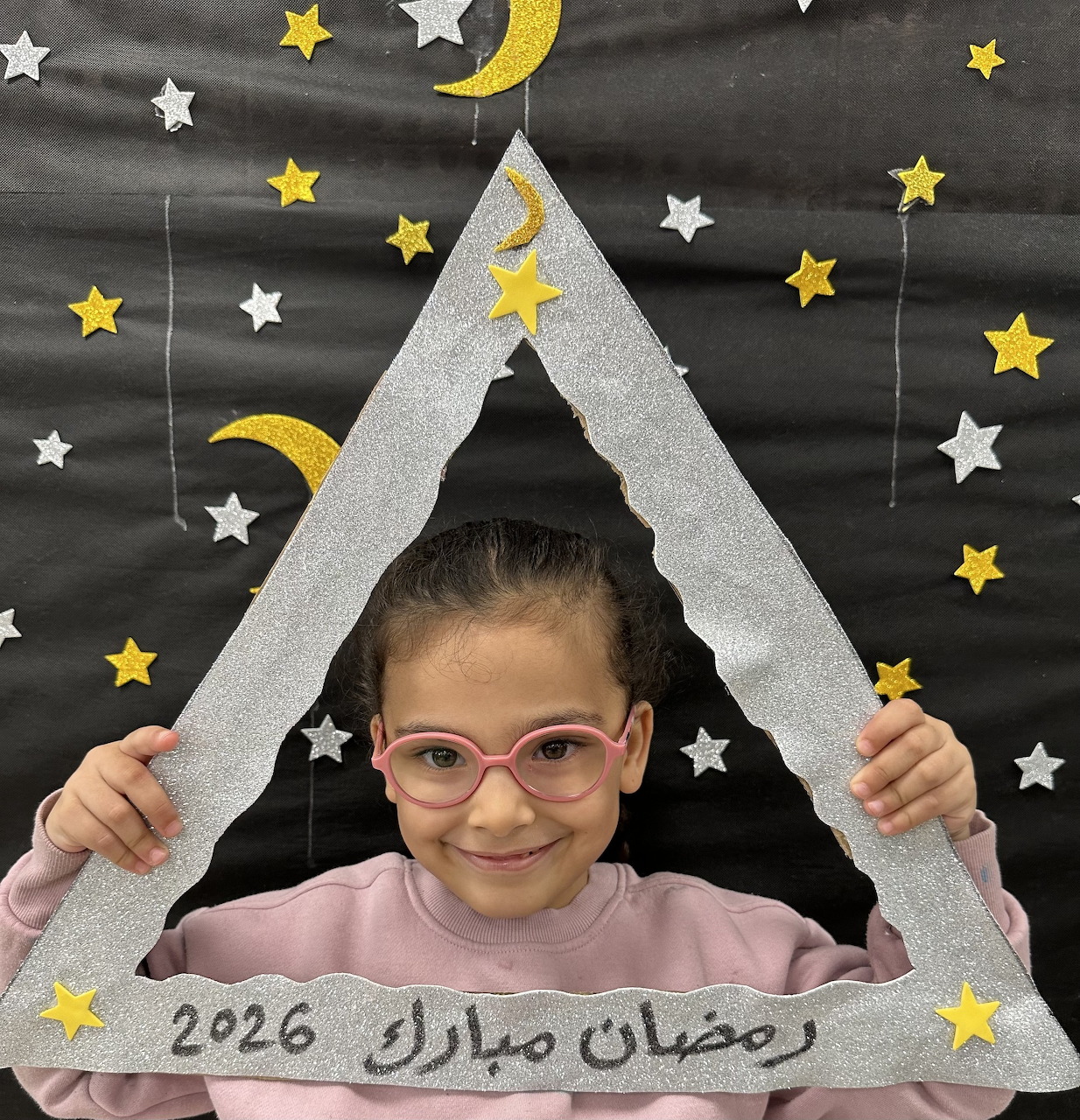 Smiling girl in pink shirt holding glittery triangular frame with moon and star decorations