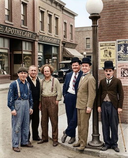 Group of eight people in vintage clothing standing on historic main street with brick buildings and apothecary shop