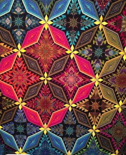 Colorful geometric quilt with star and diamond patterns in pink, blue, gold, and dark fabric