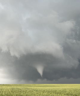 Tornado funnel cloud descending from dark storm clouds over a flat green grassland in Wyoming
