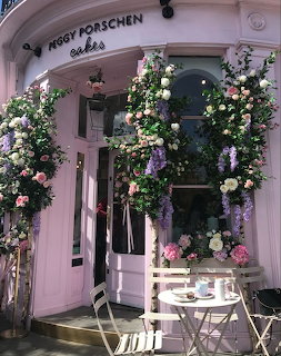 Pink cafe entrance with floral arches, white chairs, and a small outdoor table