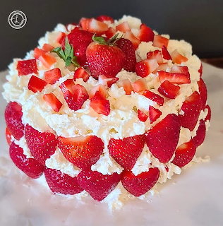 Round strawberry cake with whipped cream and fresh strawberry topping on a white plate