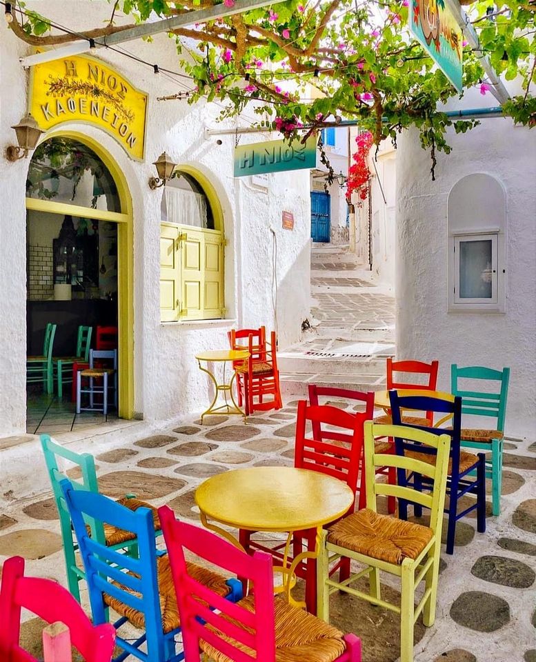 Bright multi-colored chairs and tables in white Greek island courtyard with yellow storefront