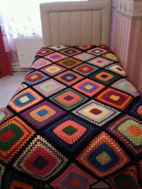 Single bed with a colorful crochet granny square blanket in a small bedroom