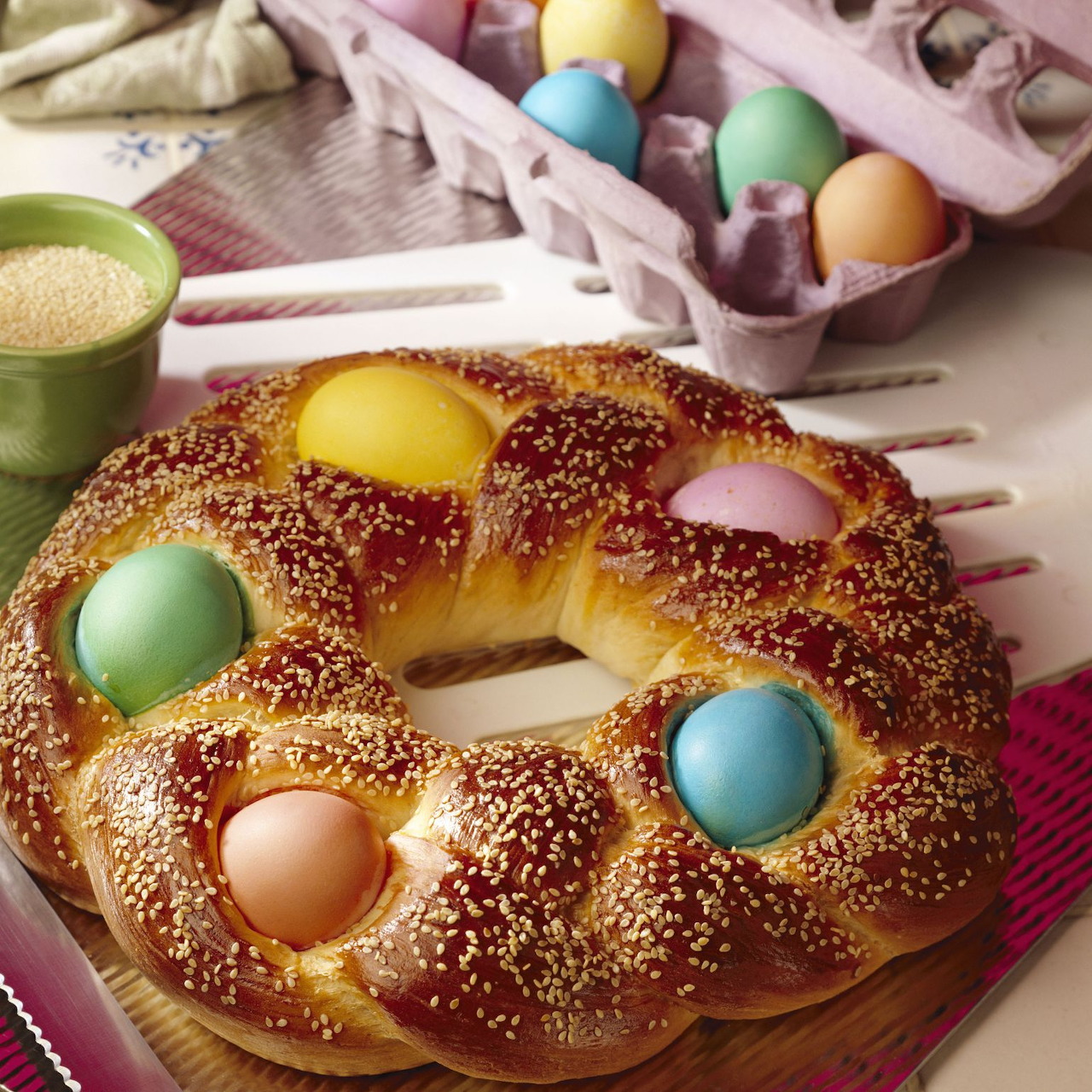 Braided Easter bread wreath topped with sesame seeds and decorated with pastel colored eggs on a pink plate
