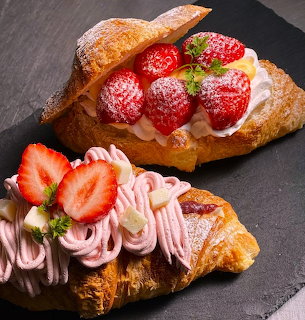Two golden croissants with strawberry cream toppings on slate board