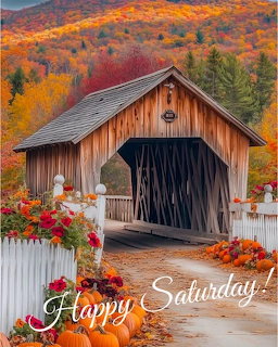 Wooden covered bridge with autumn foliage, pumpkins, and flowers along white picket fence