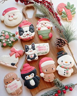 Assorted Christmas-themed decorated sugar cookies including Santa, snowman, reindeer, and penguin on wooden board