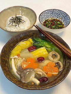 Bowl of Korean vegetable soup with mushrooms and vegetables, rice bowl, and side dish with chopsticks