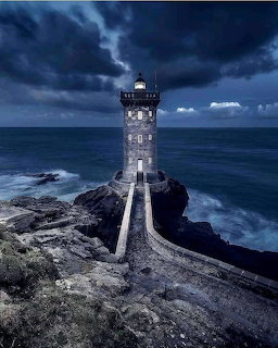 Stone lighthouse on a rocky shore under dark storm clouds by the sea