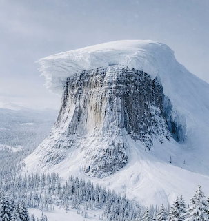 Snow-covered mountain peak with steep rocky cliff face above winter forest