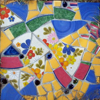 Mosaic of broken ceramic pieces with flowers and geometric shapes in blue, yellow, green, and red