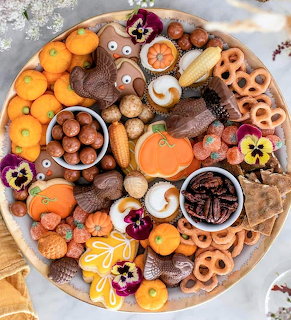 Platter of fall-themed cookies, candy and treats arranged on white plate with autumn decorations