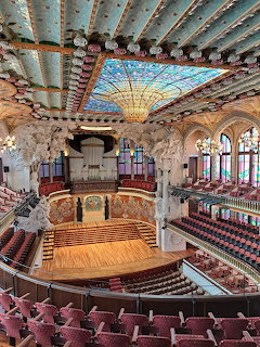 Ornate interior of Palau de la Música Catalana with stained glass ceiling, stage, and seating rows