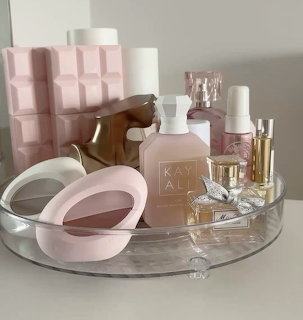 Clear round vanity tray with pink perfumes, lotions, and beauty accessories arranged neatly