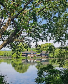 Traditional Chinese pavilion on a lake shore reflected in calm water, framed by green trees