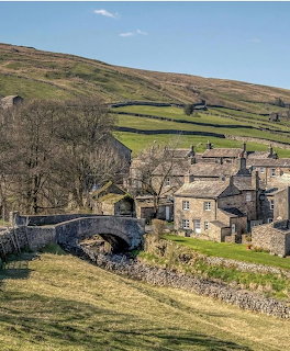 Stone arch bridge and traditional cottages in a Yorkshire Dales valley with green hills and dry stone walls
