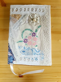 Handmade journal with vintage lace, floral embroidery, and decorative fabrics on wooden surface