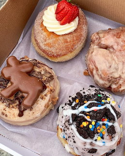 Four gourmet donuts in a white box with various toppings including strawberry, chocolate, and sprinkles