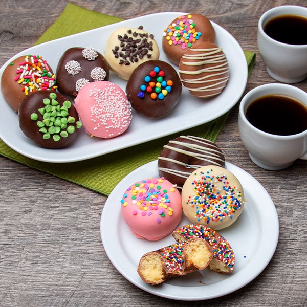 Assorted decorated cookies with colorful toppings on white plates next to coffee cups