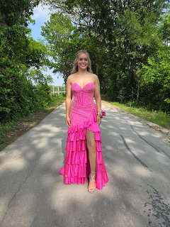 Woman in a bright pink prom dress standing on a tree-lined road