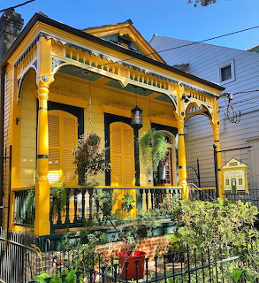 Vibrant yellow Victorian house with decorative white trim and front porch behind wrought iron fence