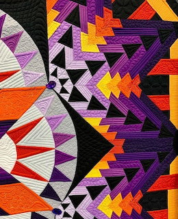 Colorful geometric quilt with triangular patterns in purple, orange, yellow, black and white
