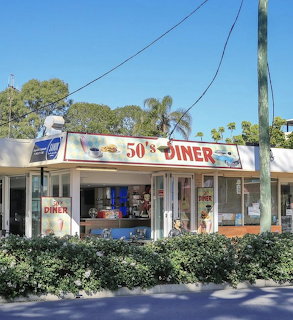 Retro 50s Diner restaurant with red and white signage, glass windows, and palm trees on a sunny day