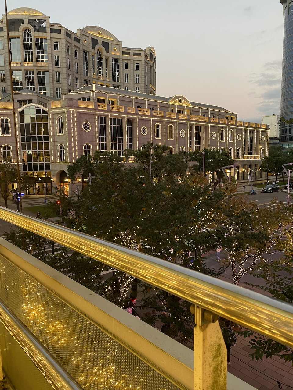 Bellavita shopping mall in Taipei at dusk, European-style facade with trees and golden railing