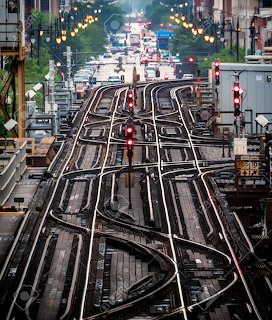 Elevated train tracks with intersecting rail switches and signal lights above city streets