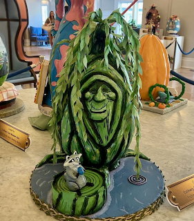 Indoor display of a stylized tree face with hanging green leaves and a small raccoon figure