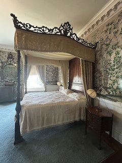 Vintage bedroom with ornate canopy bed, patterned wallpaper, and a small table with a globe