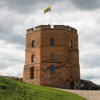 Medieval brick tower with Lithuanian flag on hilltop under cloudy sky