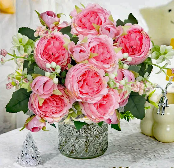 Pink rose bouquet in a glass vase on a rustic table with a small cream pitcher