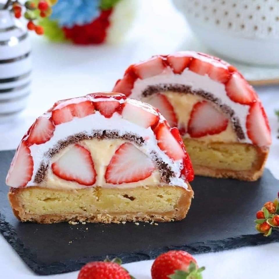 Two slices of strawberry cream roll cake with vanilla sponge, white cream filling, and fresh strawberry slices on dark slate