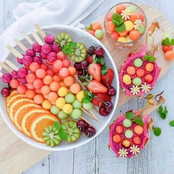 Rainbow fruit platter with colorful melon balls, grapes, cherries and kiwi arranged in gradient from pink to green