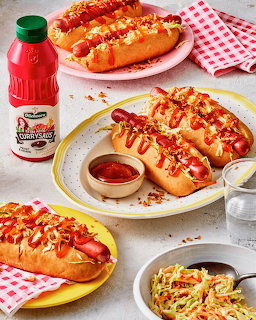 Three hotdogs with curry sauce, mustard, crispy onions, and coleslaw on plates with red checkered napkin