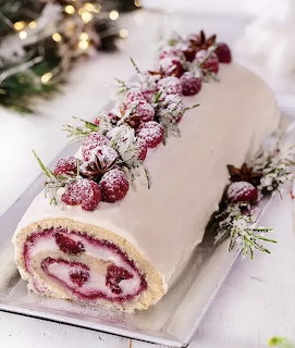 White frosted yule log cake topped with sugared red berries and pine greenery
