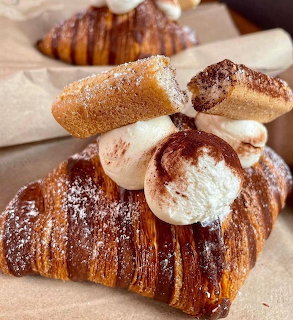 Assorted baked pastries including croissants and cream-filled desserts with powdered sugar and cinnamon on parchment
