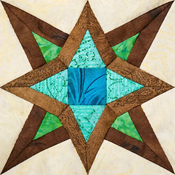 Geometric star quilt block with brown points, turquoise center with blue floral design, and green triangles