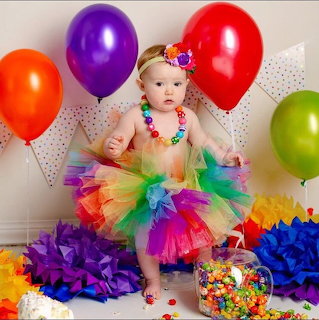 Baby girl wearing colorful rainbow tutu surrounded by balloons and party decorations