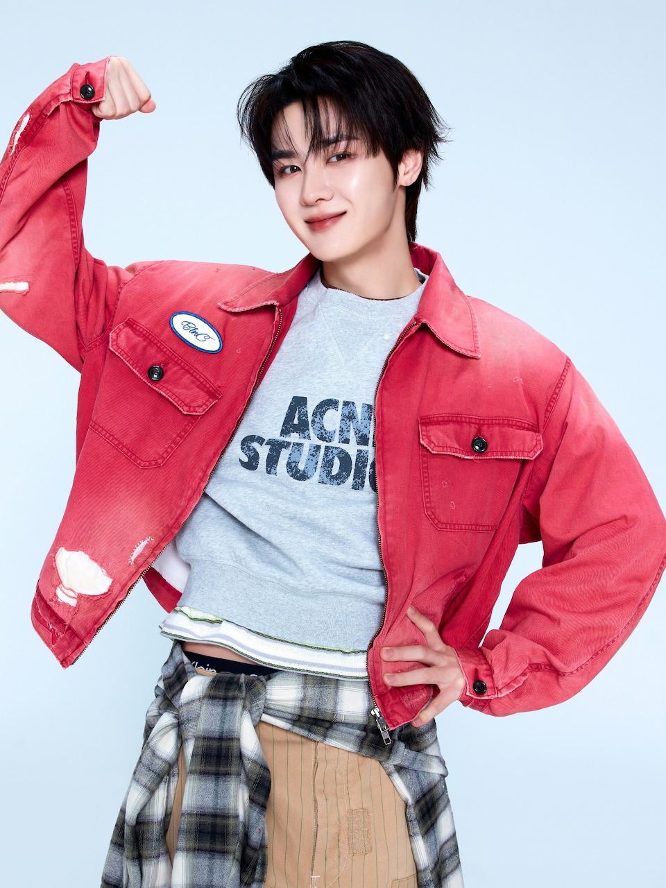 Young Asian man flexing in a red denim jacket and Acne Studios t-shirt on a light blue background