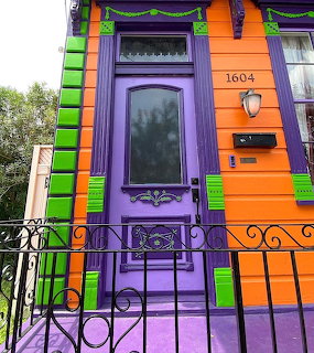 Bright purple door with ornate details on a colorful green and orange painted house facade with iron fence