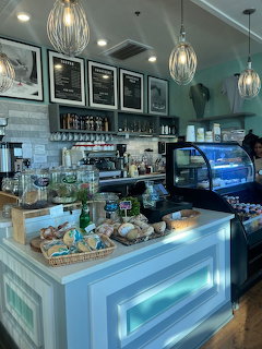 Bright cafe counter with blue paneling, glass pastry display, espresso machine, and pendant lights