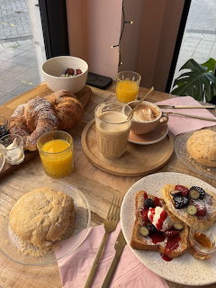 Brunch table with croissants, coffee cup, orange juice, and assorted pastries on wooden boards