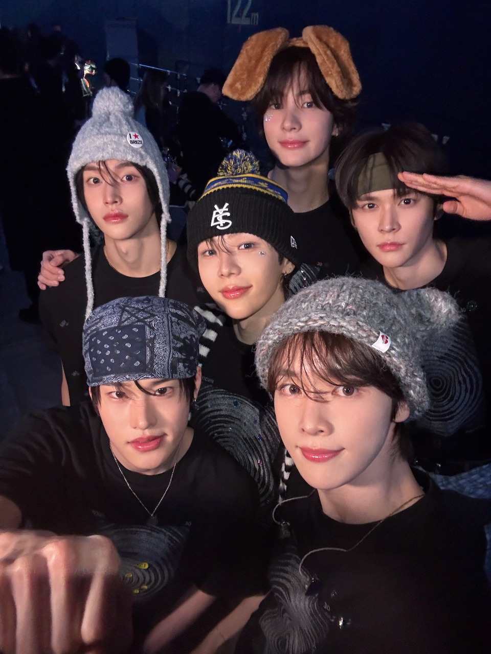Six young men wearing winter hats and dark clothing in a close group portrait